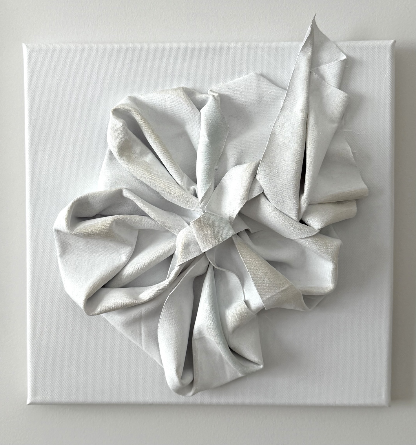 Bloom, Sculptural white fabric petals forming a flower on a white canvas